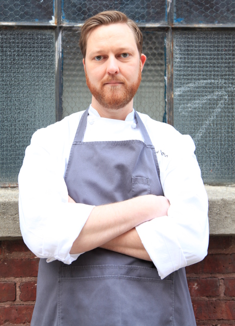 close up shot of chef Jeffrey against windows/bricks, arms crossed, serious look