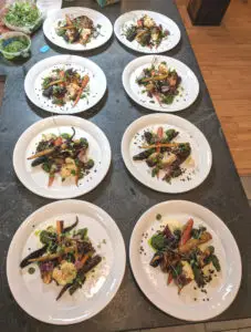 8 plates lined up with main course of vegetables on them